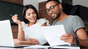 A young couple reviews paperwork at a desk and considers Contactless Mortgage Closings
