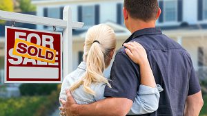 A couple embracing in front of a sold sign and large home with a headline that reads Buyer in a Seller's Market