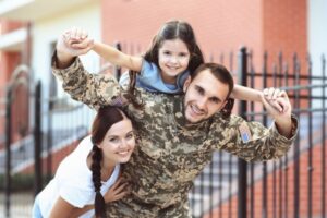 A veteran embraces his family outside home purchased with VA Loans